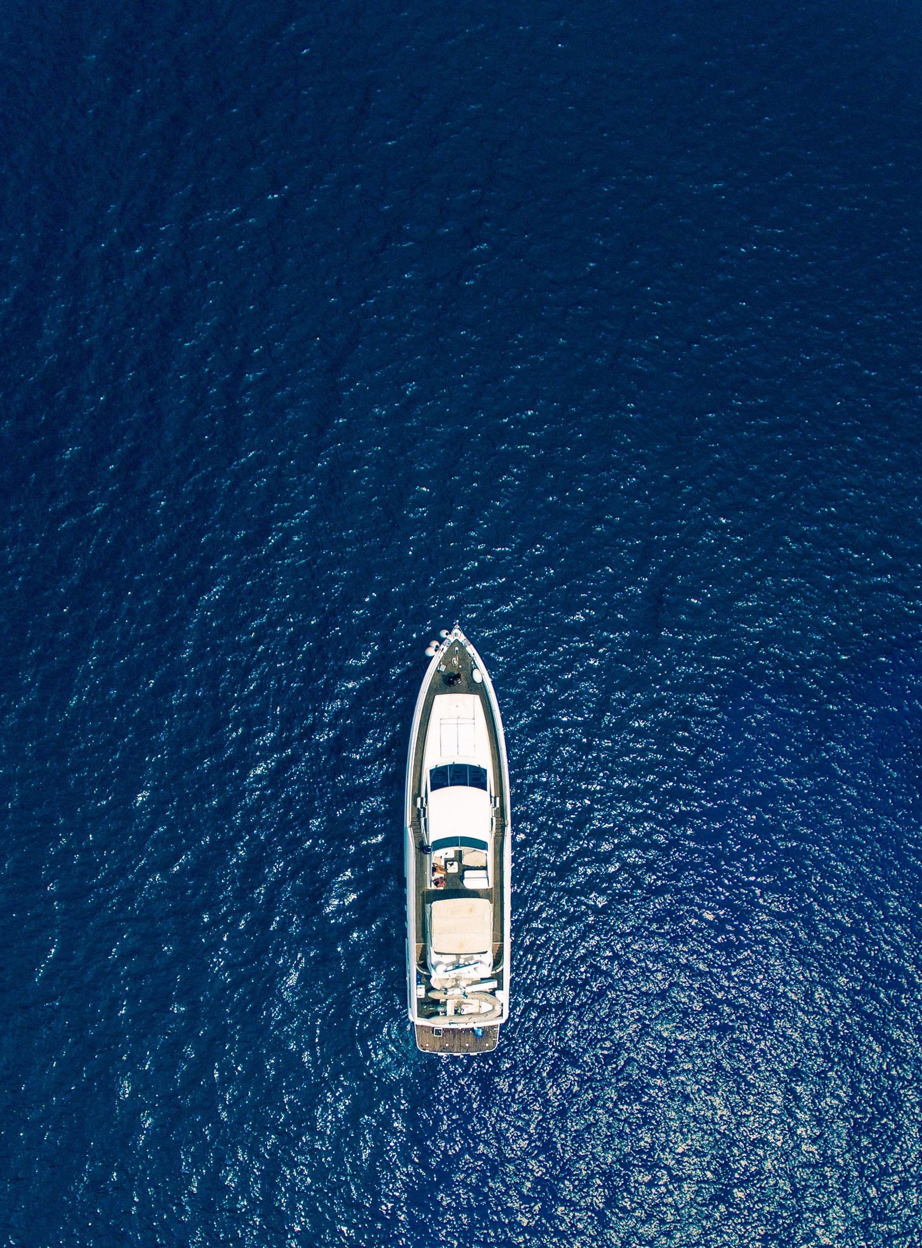 Белая моторная яхта в открытом море, вид сверху на глубокую синюю воду